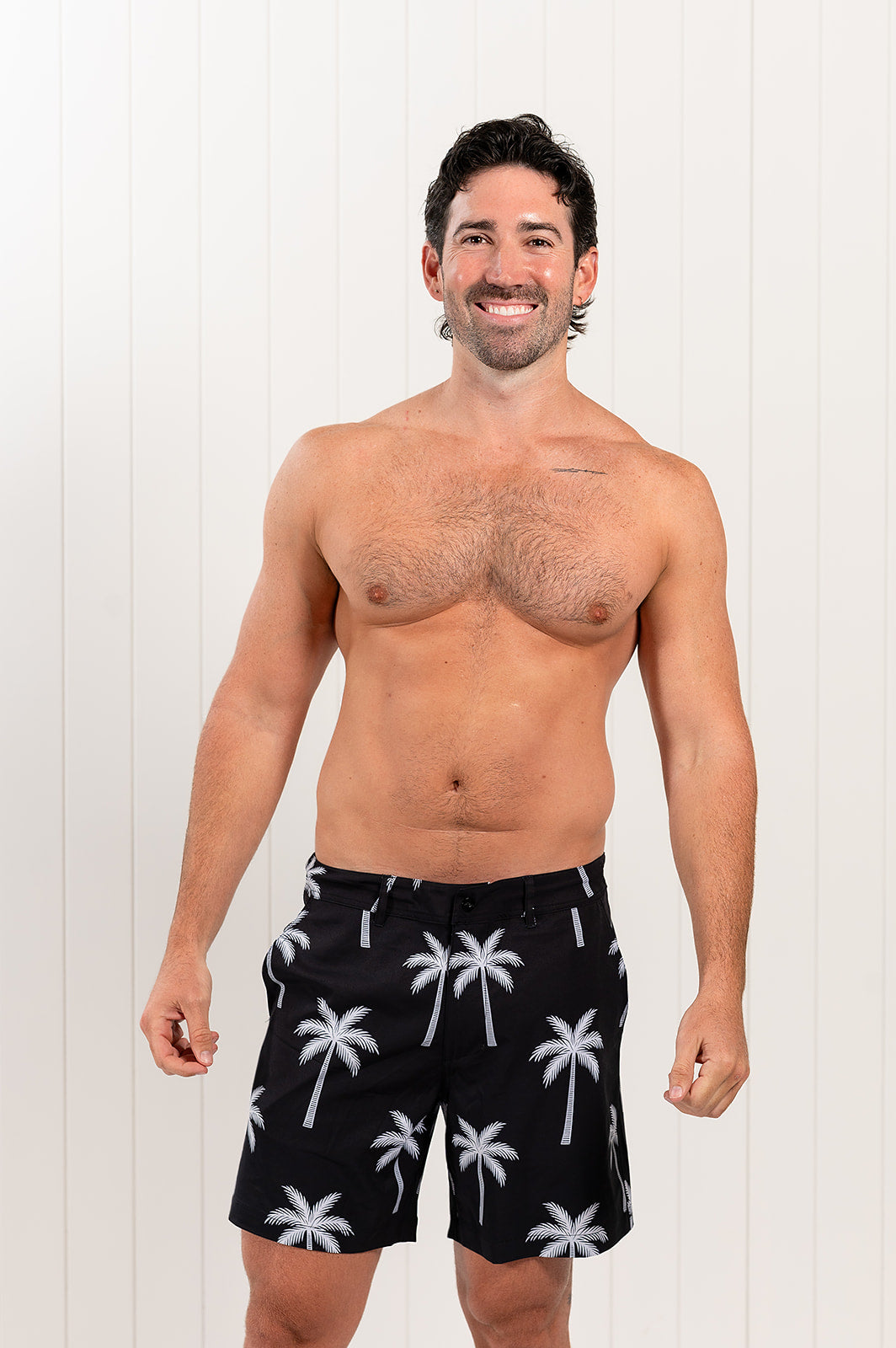 Man wearing black swim shorts with palm tree pattern against a white background